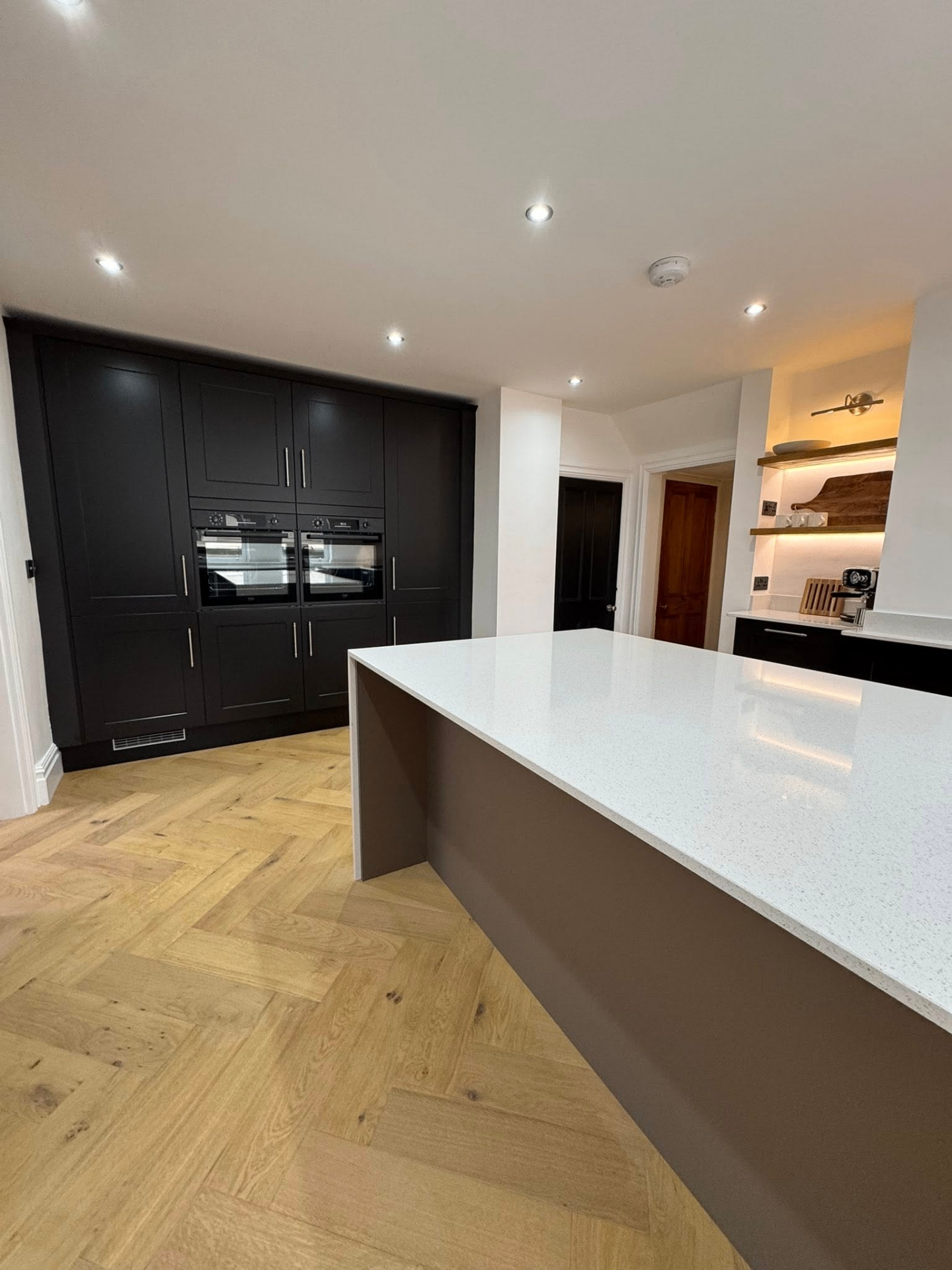 Black shaker kitchen with integrated ovens and herringbone flooring